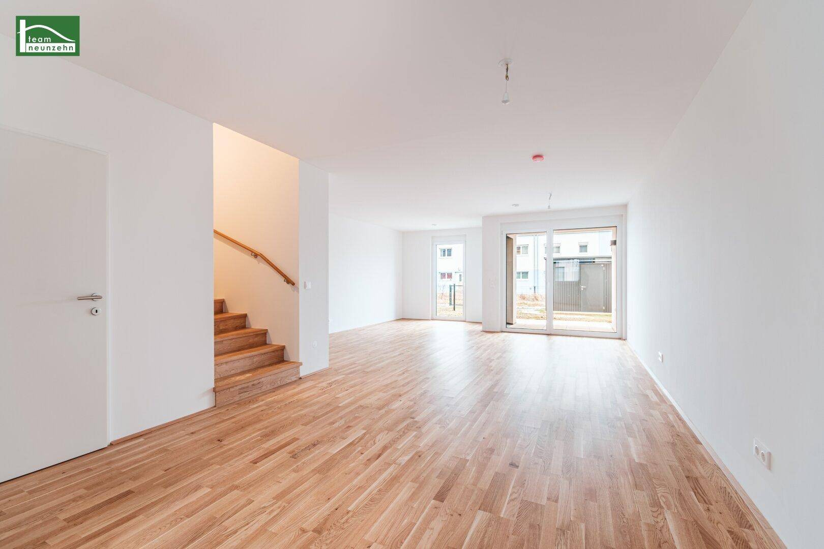 Geräumiger, heller Wohnbereich mit Parkettboden, Treppe und Zugang zur Terrasse.