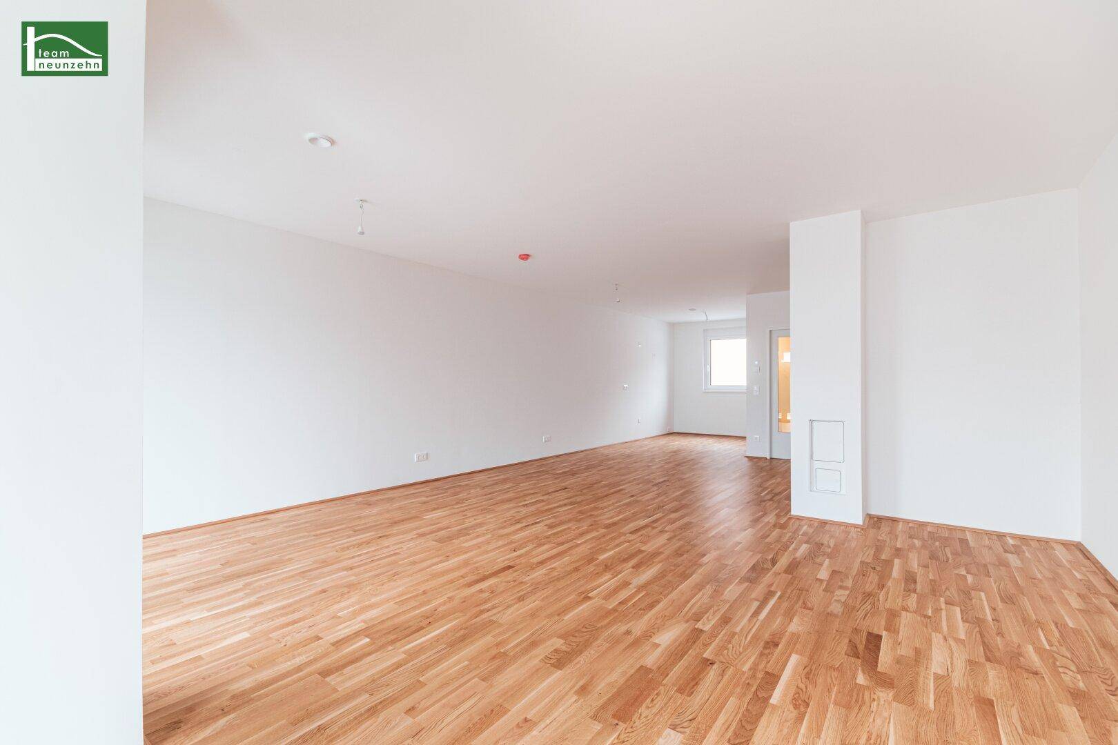 Weitläufiger, heller Wohnbereich mit Parkettboden und viel Tageslicht, ideal für flexible Einrichtung.