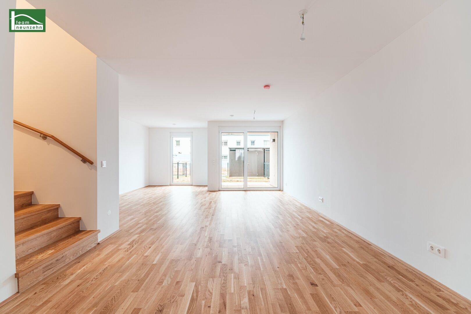 Geräumiger, heller Wohnbereich mit Holztreppe und Zugang zur Terrasse oder Garten.