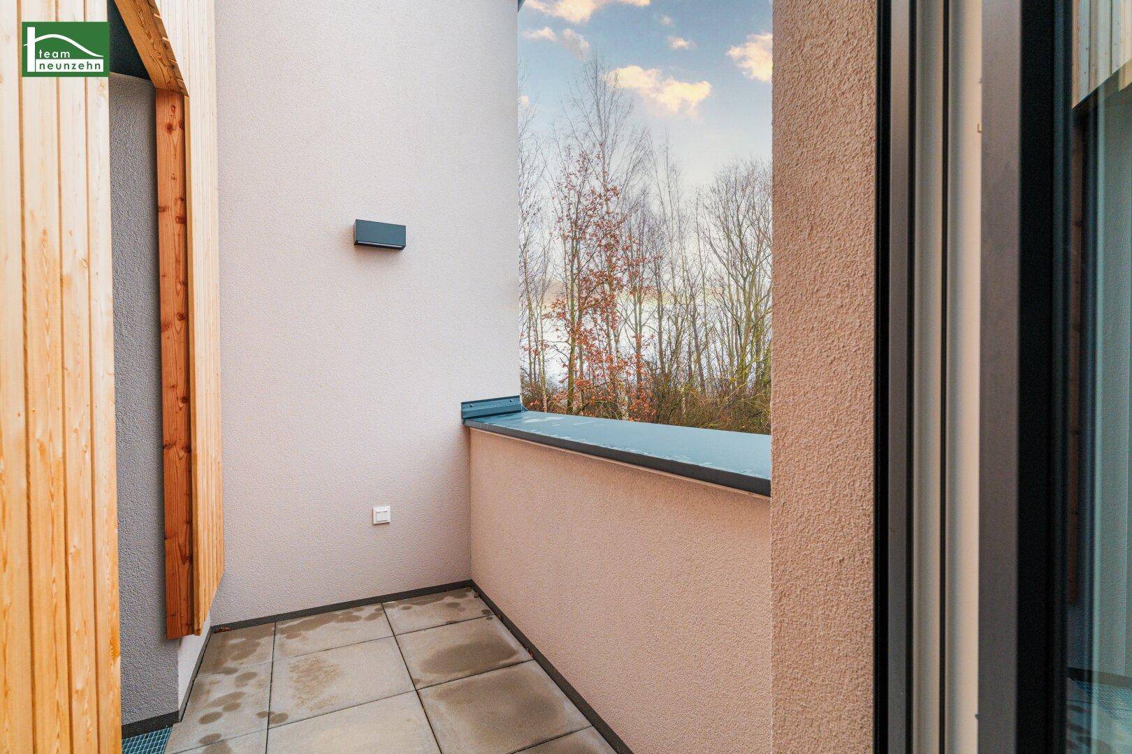 Kleiner, gefliester Balkon mit Blick auf Bäume und den Himmel.