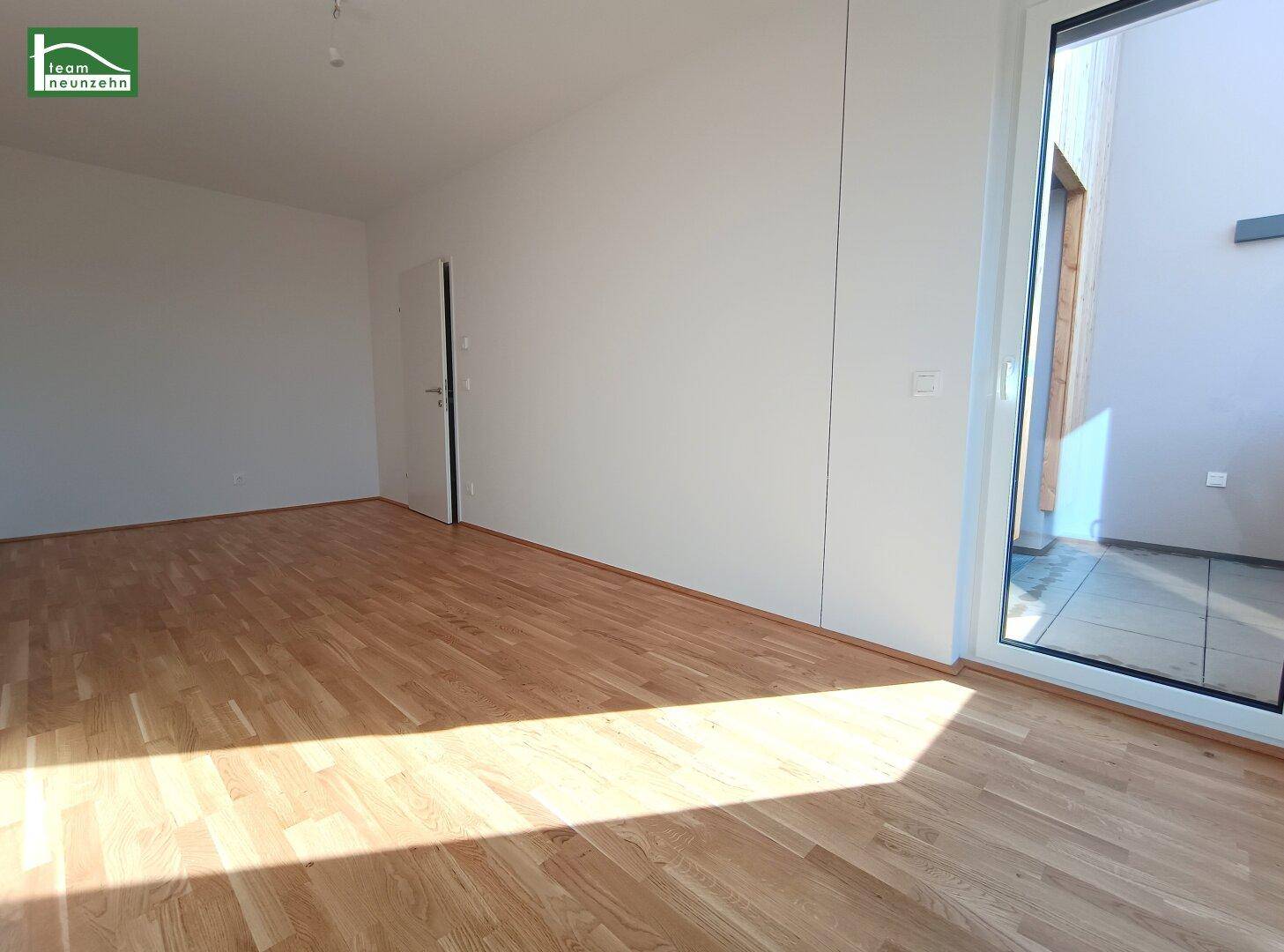 Heller Raum mit Holzboden und großem Fenster, das Zugang zu einem Außenbereich bietet.