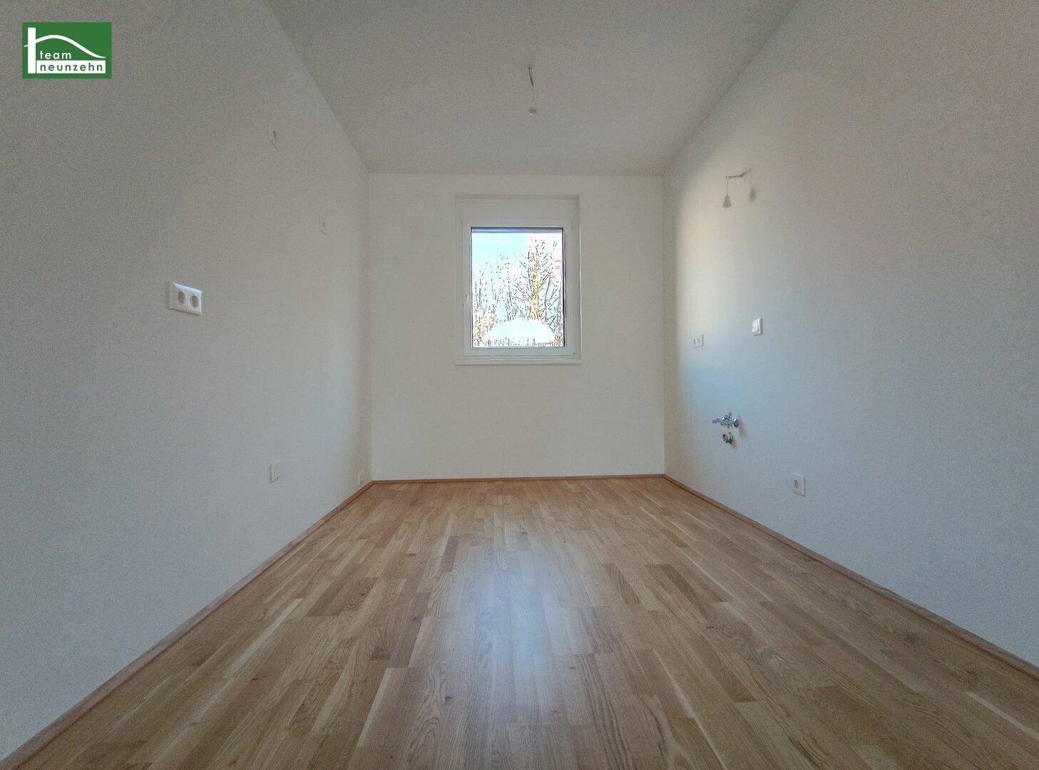 Helles Schlafzimmer mit Holzboden und einem Fenster mit Blick ins Grüne.
