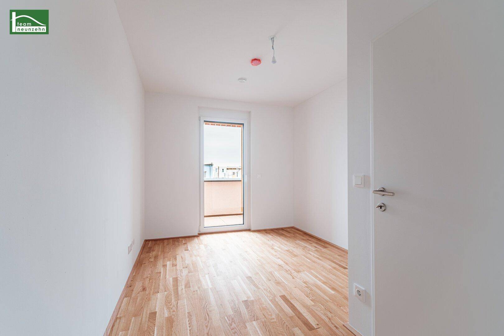 Helles Schlafzimmer mit Parkettboden und Zugang zu einem kleinen Balkon.