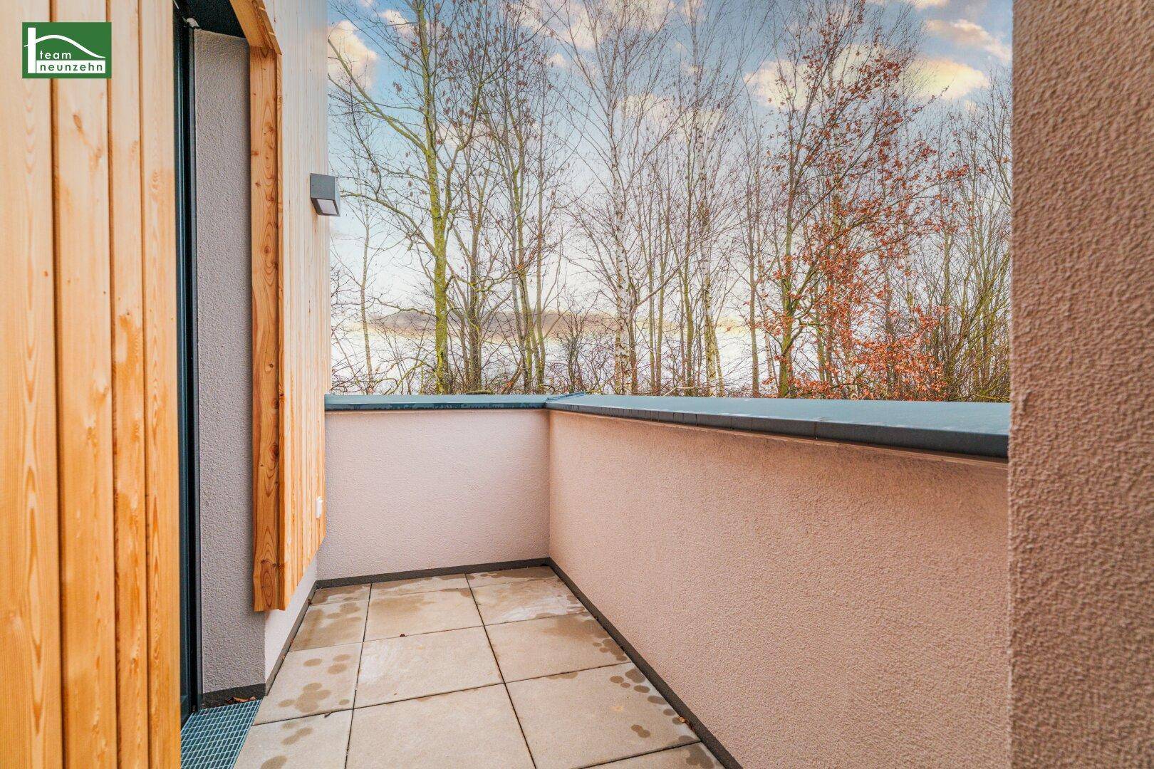 Kleiner Balkon mit Fliesenboden und Blick auf Bäume und den Himmel.