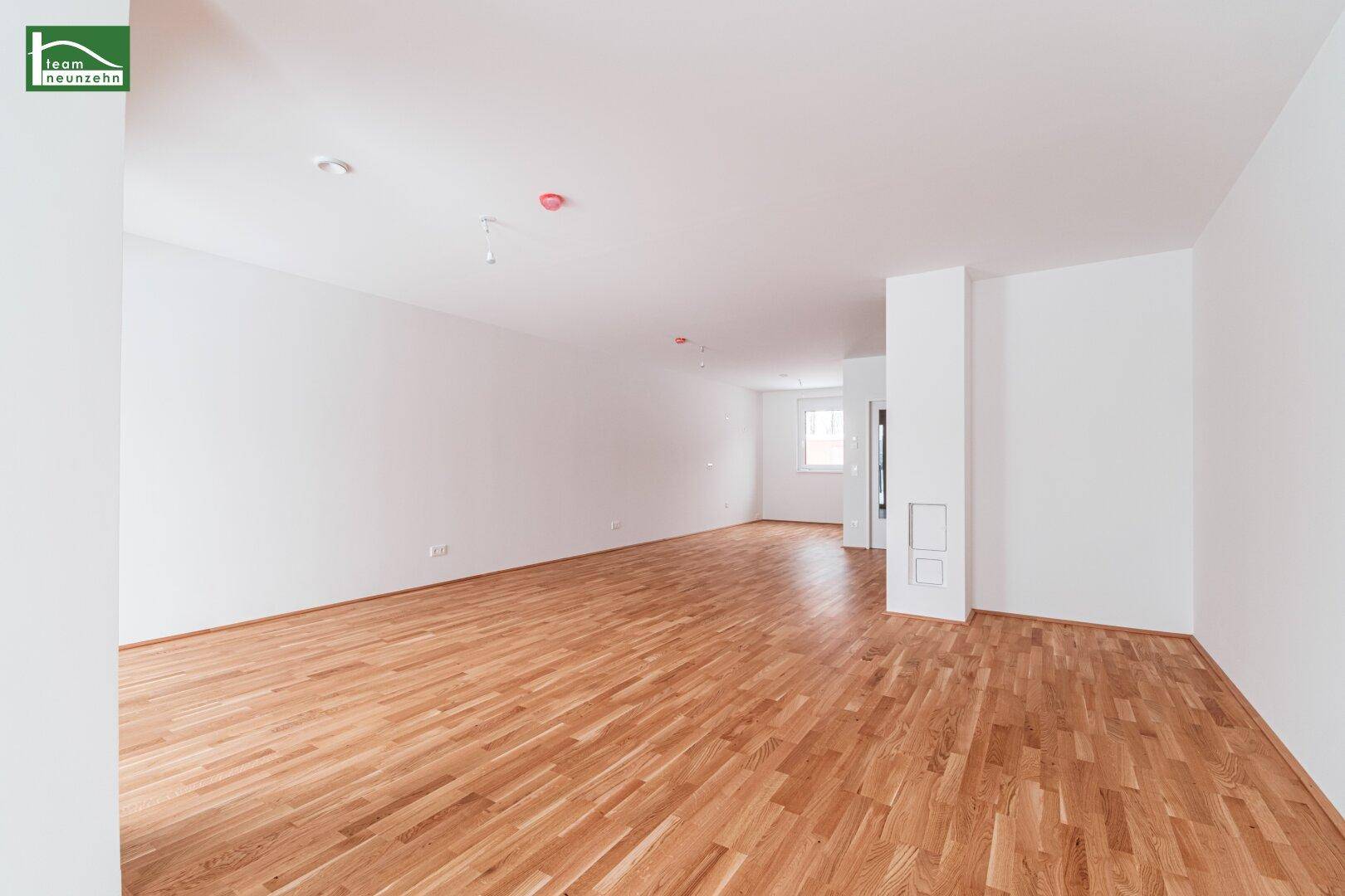 Geräumiger, heller Wohnbereich mit Holzboden und schlichten weißen Wänden, ideal für moderne Einrichtung.