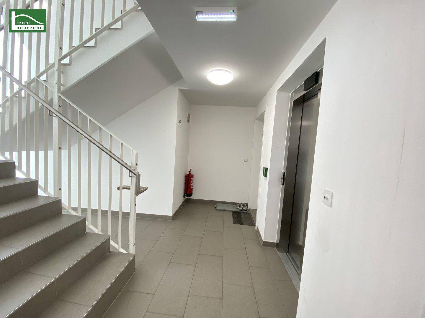 Heller Eingangsbereich mit Treppenhaus und modernem Aufzug, der alle Etagen erschließt.