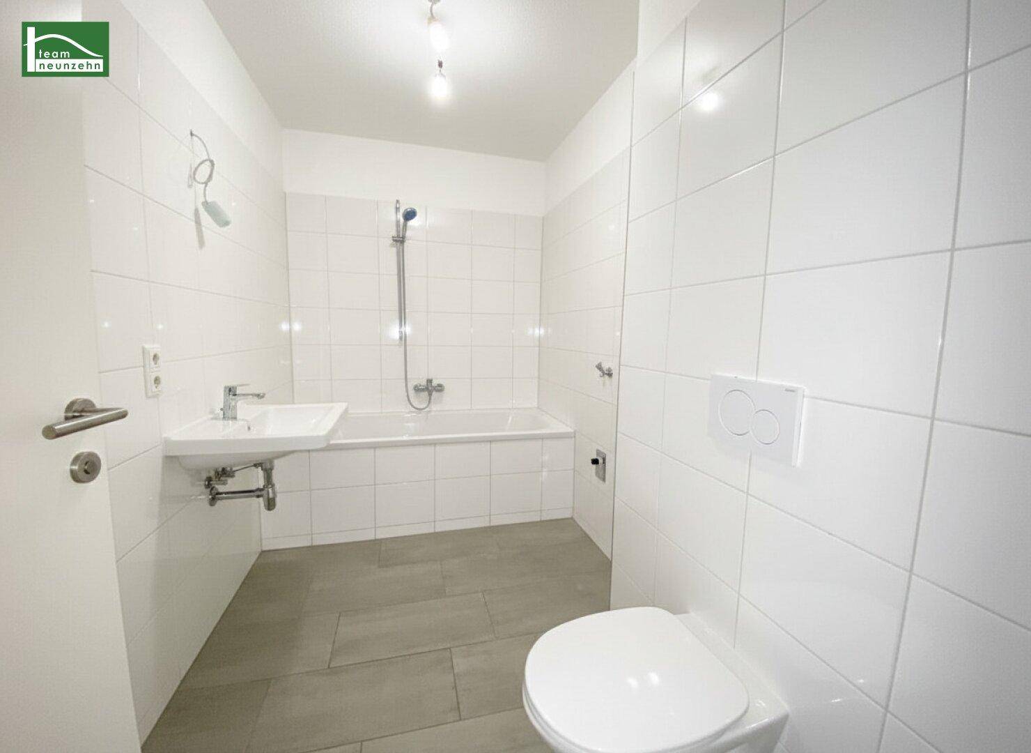 Modernes Badezimmer mit weißen Fliesen, Badewanne mit Duschfunktion und wandhängendem WC.