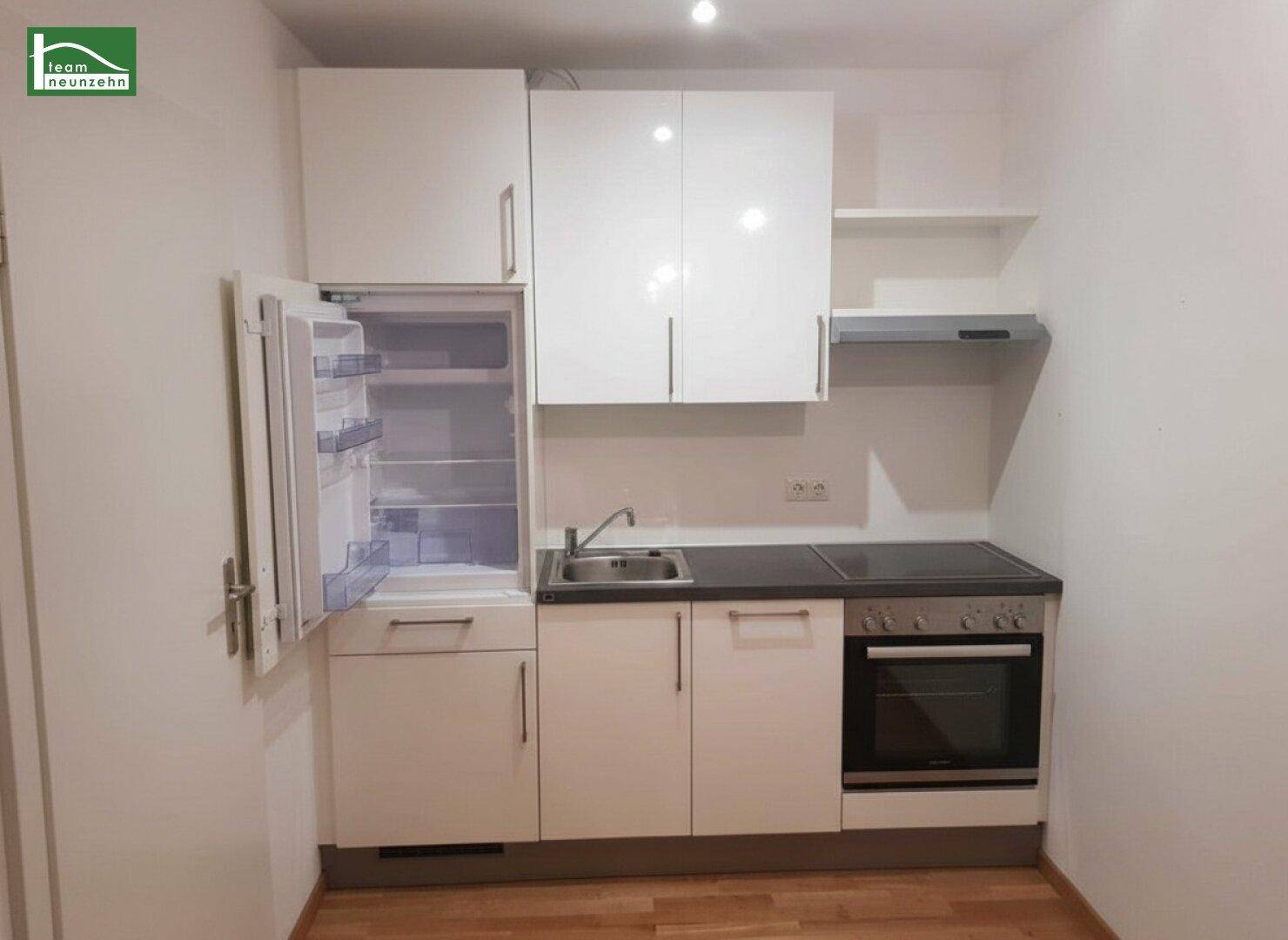 Kompakte Einbauküche mit weißen Hochglanzfronten, integriertem Kühlschrank und Kochfeld.