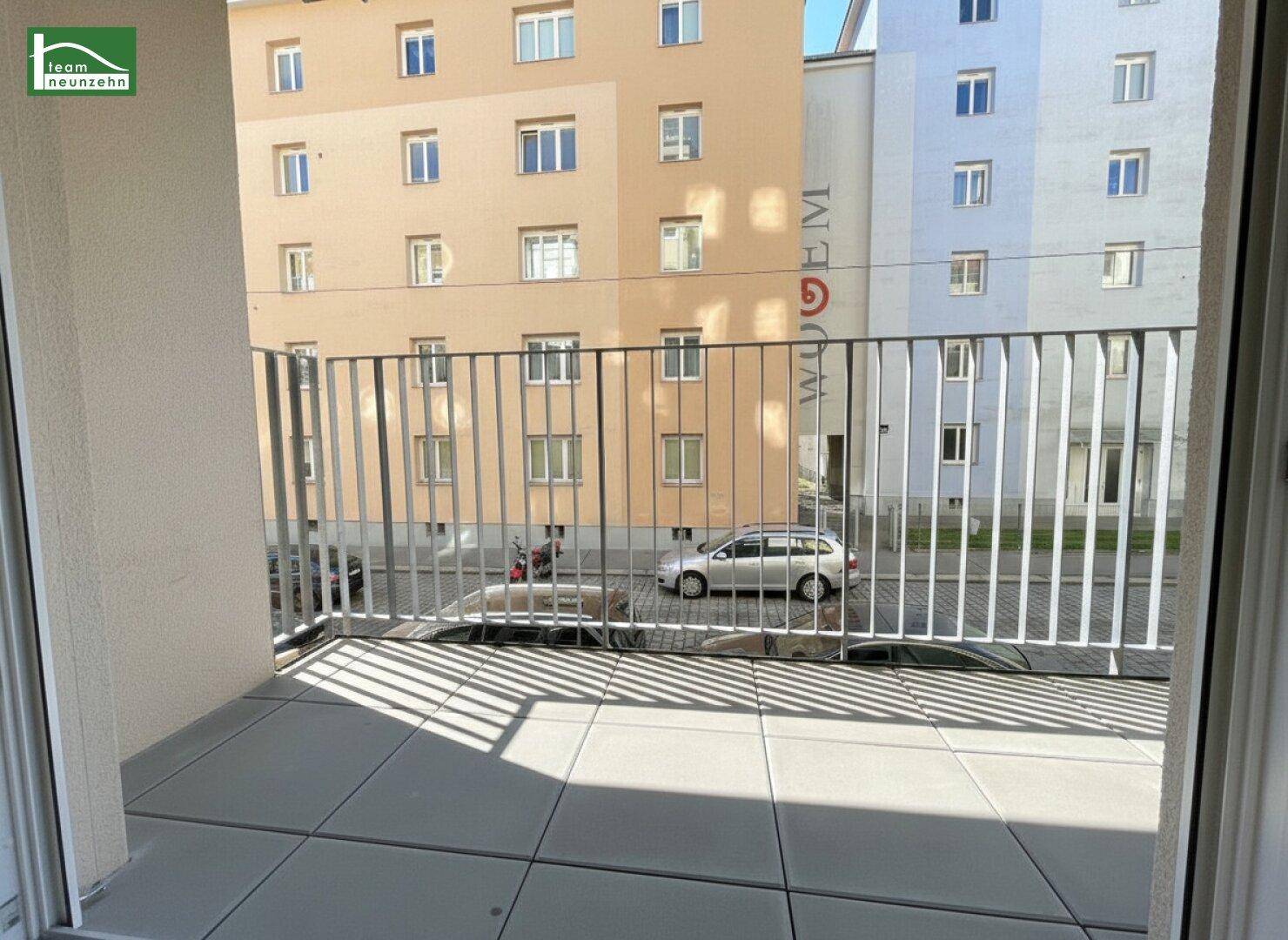 Balkon mit Fliesenboden und Metallgeländer, bietet einen Blick auf die gegenüberliegenden Gebäude und die Straße.