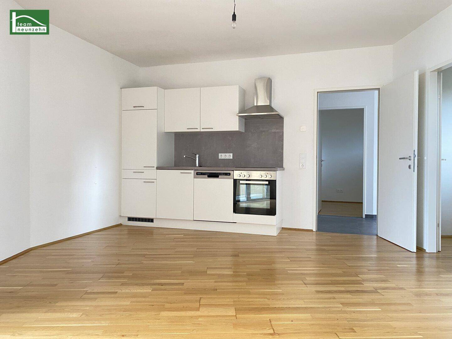 Moderne Küchenzeile mit weißen Schränken, integriertem Backofen und Dunstabzugshaube in hellem Raum.