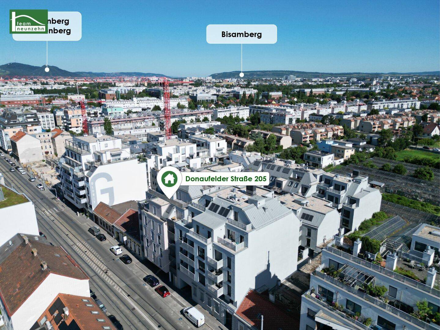Weitläufige Luftaufnahme der Stadt mit dem Bisamberg im Hintergrund und der Donaufelder Straße.