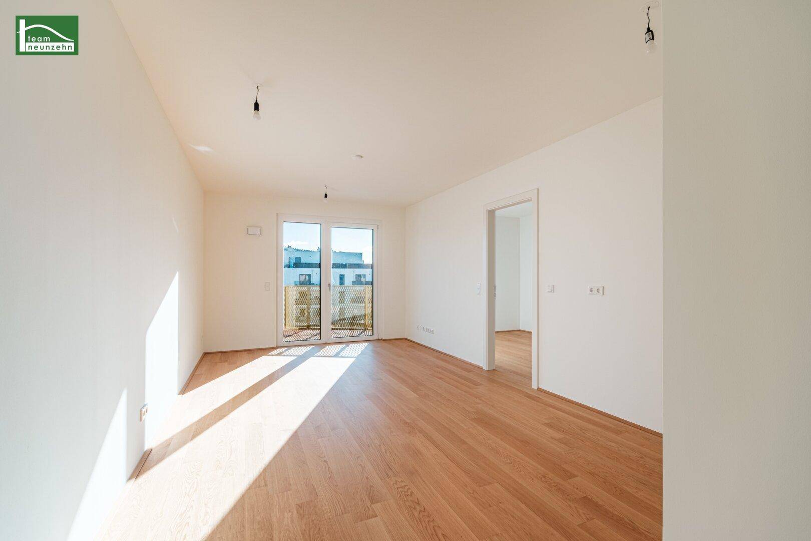Lichtdurchfluteter Wohnbereich mit Holzboden und großen Schiebetüren zum Balkon.
