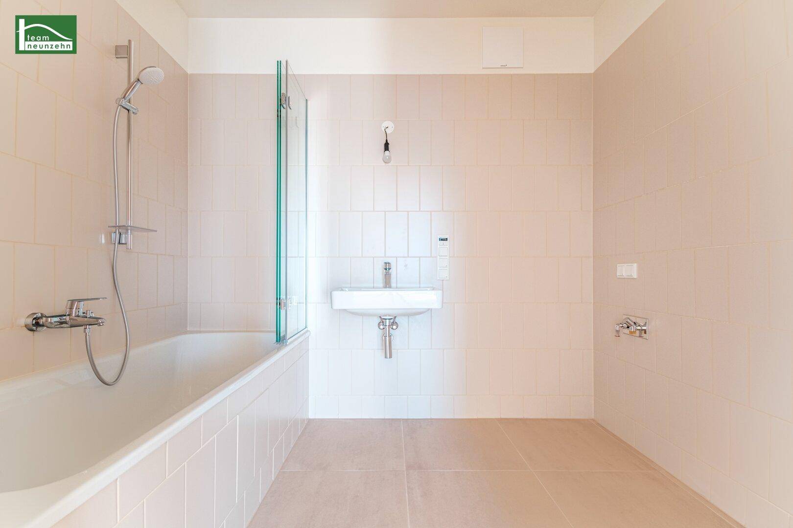 Modernes Badezimmer mit Badewanne, Duschabtrennung und Waschbecken in hellen Fliesen.