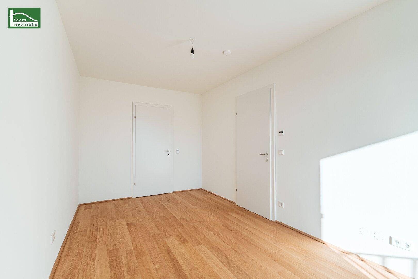 Leerer Raum mit hellem Holzboden und zwei Türen, geeignet als Schlaf- oder Arbeitszimmer.