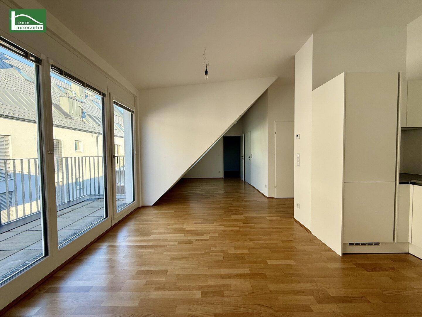 Geräumiger Wohnbereich mit großen Fenstern, Holzboden und Zugang zum Balkon.