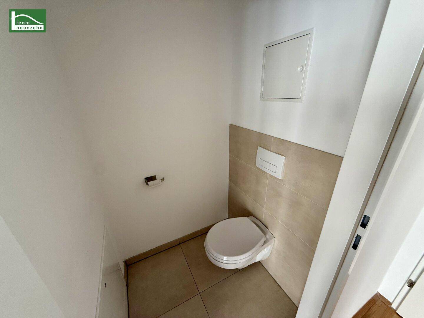 Separates WC mit wandhängender Toilette und Fliesenboden.
