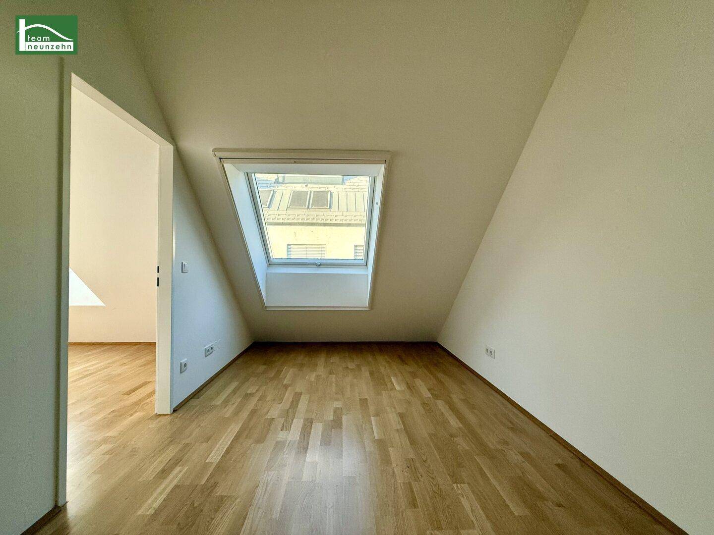 Helles Zimmer im Dachgeschoss mit Dachfenster und Holzboden.