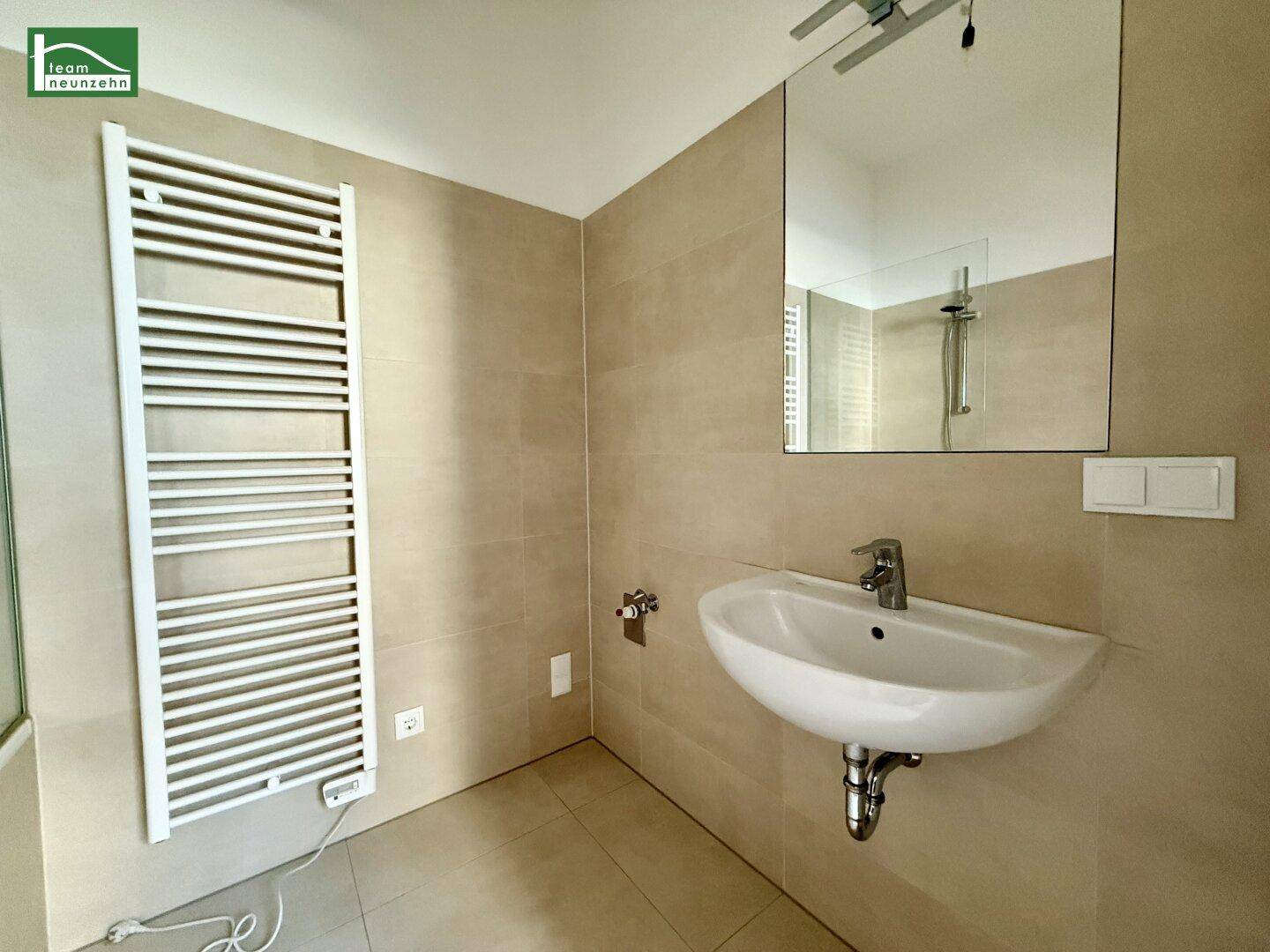 Modernes Badezimmer mit Einzelwaschbecken, großem Spiegel und beheiztem Handtuchhalter.