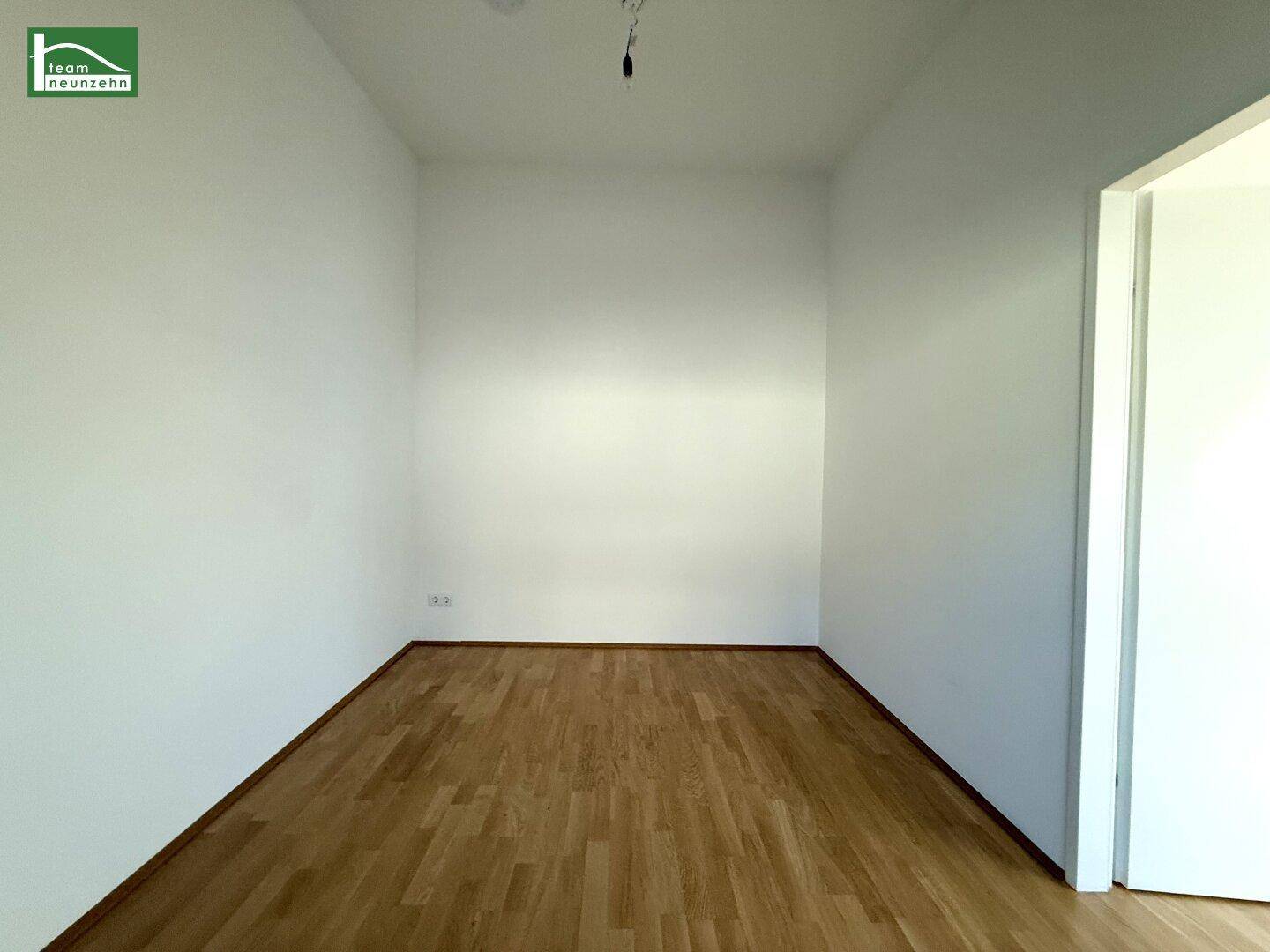 Leerer, heller Raum mit Holzboden und weißen Wänden, vielseitig nutzbar.