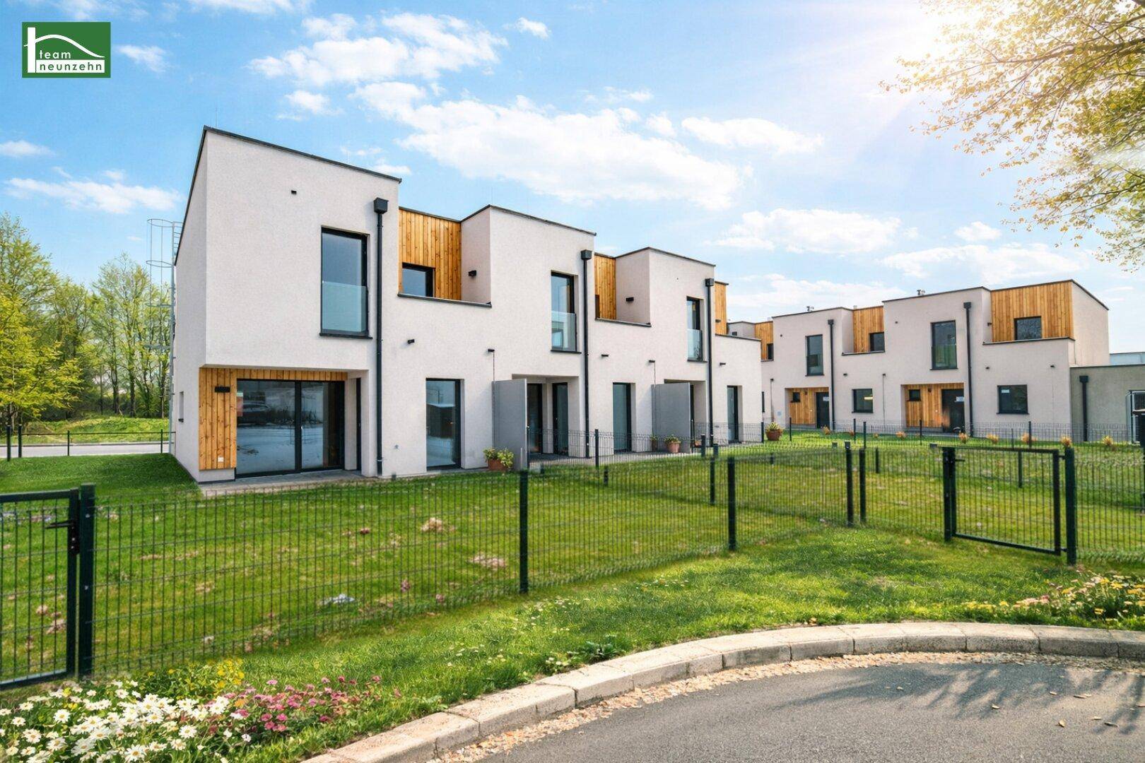 Moderne Reihenhäuser mit weißer Fassade und Holzelementen, umgeben von grünen Gärten und einem Gehweg.