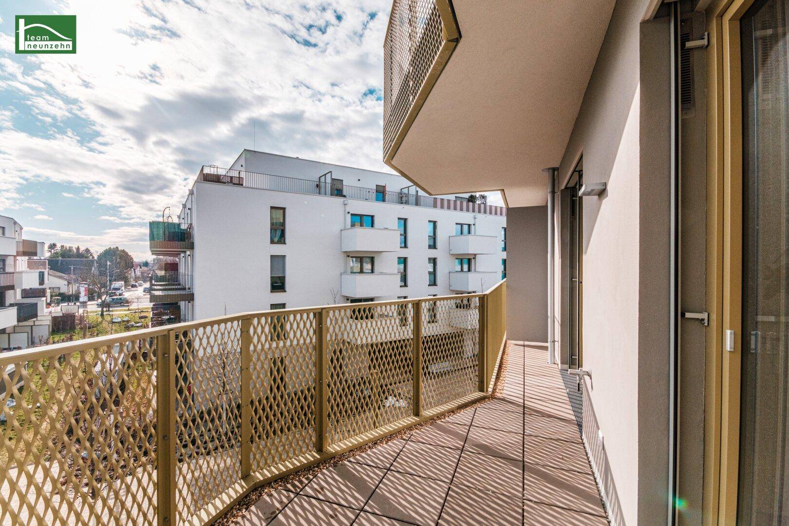 Langer Balkon mit Gittergeländer und Blick auf die Nachbargebäude, sonnig und offen gestaltet.