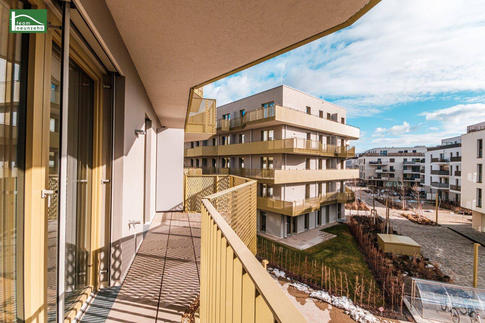 Langer Balkon mit modernem Metallgeländer und weitem Blick auf die Wohnanlage unter blauem Himmel.