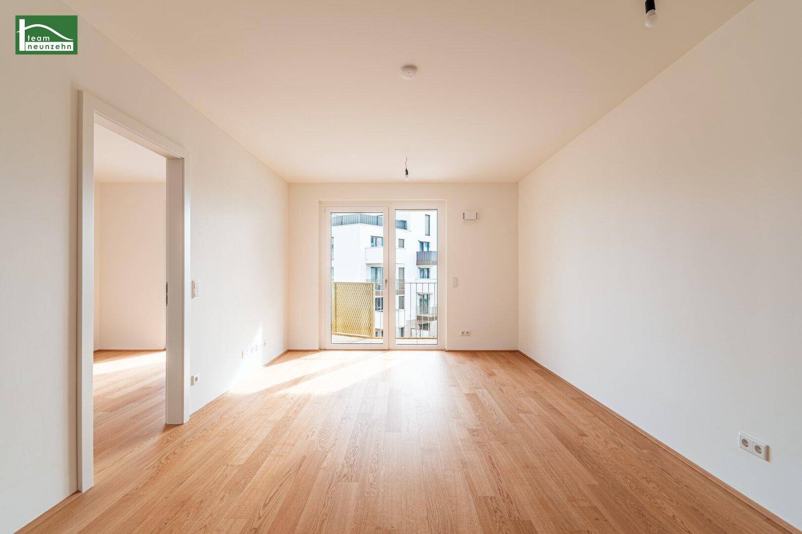 Helles, leeres Wohnzimmer mit hellem Parkettboden und Zugang zu einem Balkon.