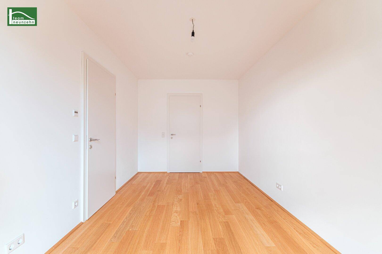 Leeres Schlafzimmer mit hellem Parkettboden und zwei weißen Türen.