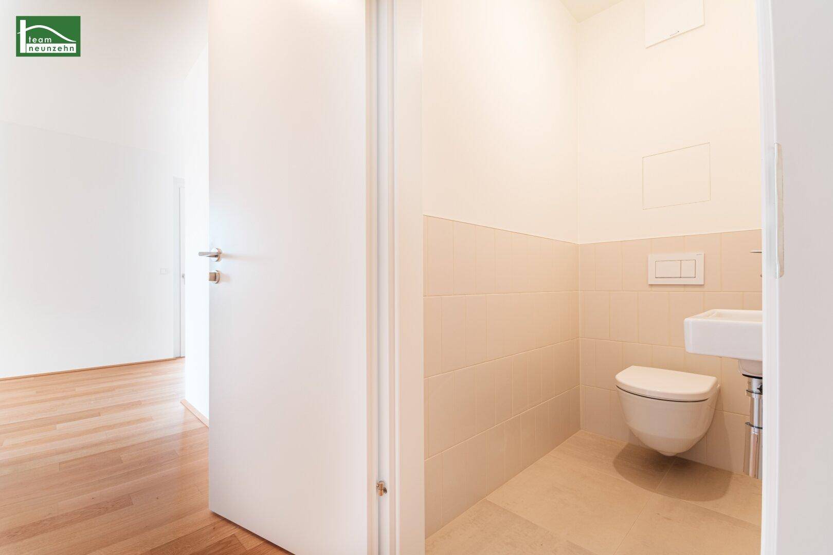 Separates Gäste-WC mit wandhängender Toilette, kleinem Waschbecken und hellen Fliesen.