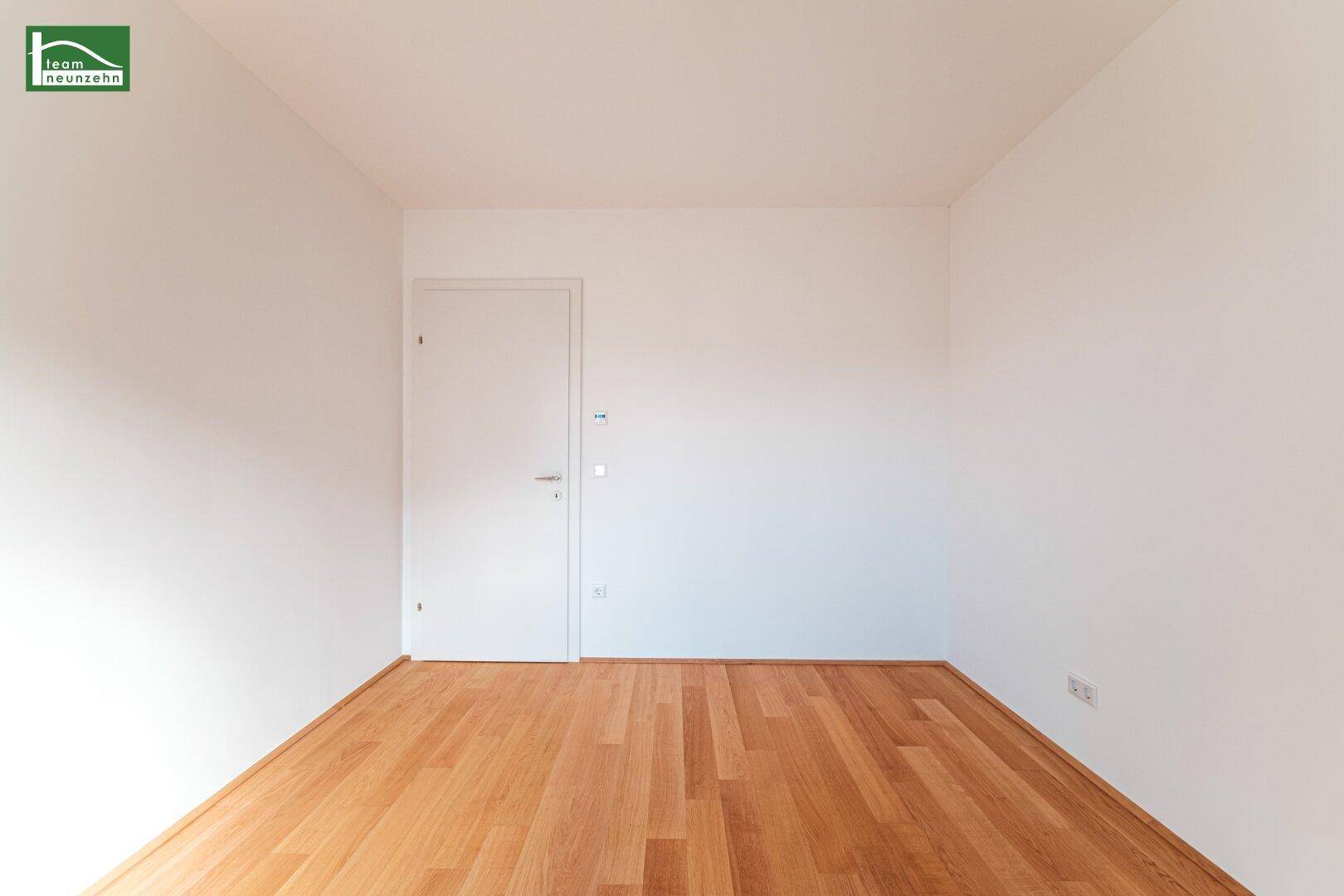 Leeres Zimmer mit Holzboden und weißer Tür, ideal als Schlafzimmer.