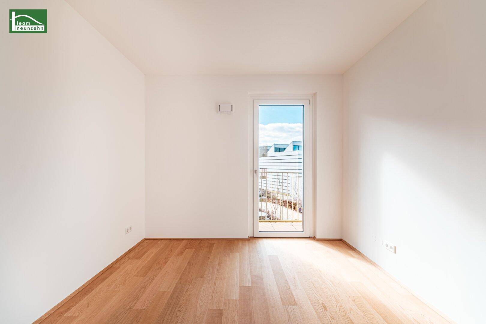 Helles Schlafzimmer mit Holzboden und Zugang zu einem kleinen Balkon.