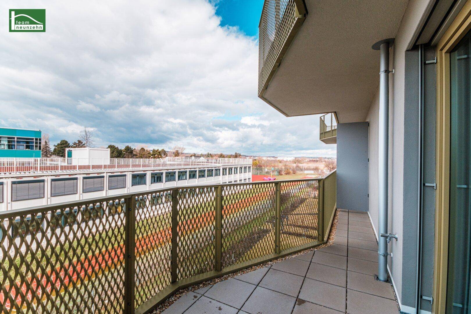 Geräumiger Balkon mit Metallgeländer und Blick auf die Umgebung unter bewölktem Himmel.