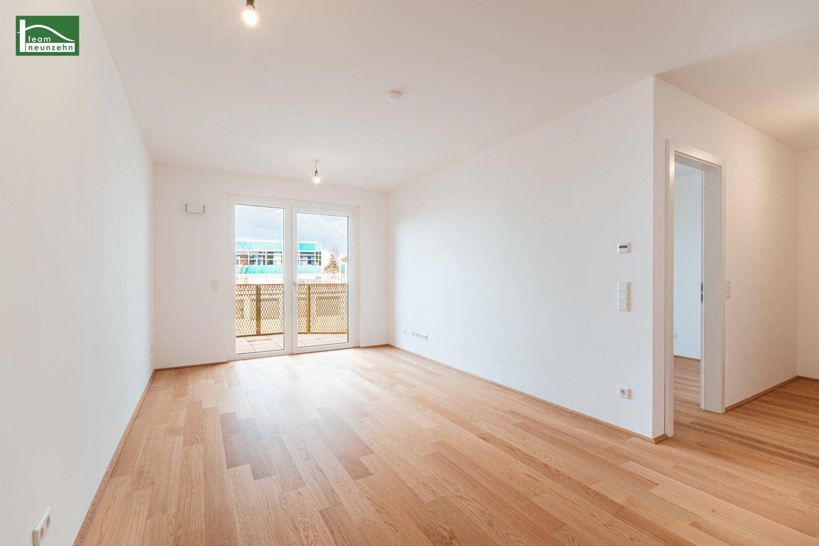 Geräumiges, leeres Wohn-Esszimmer mit hellem Holzboden und Zugang zum Balkon.