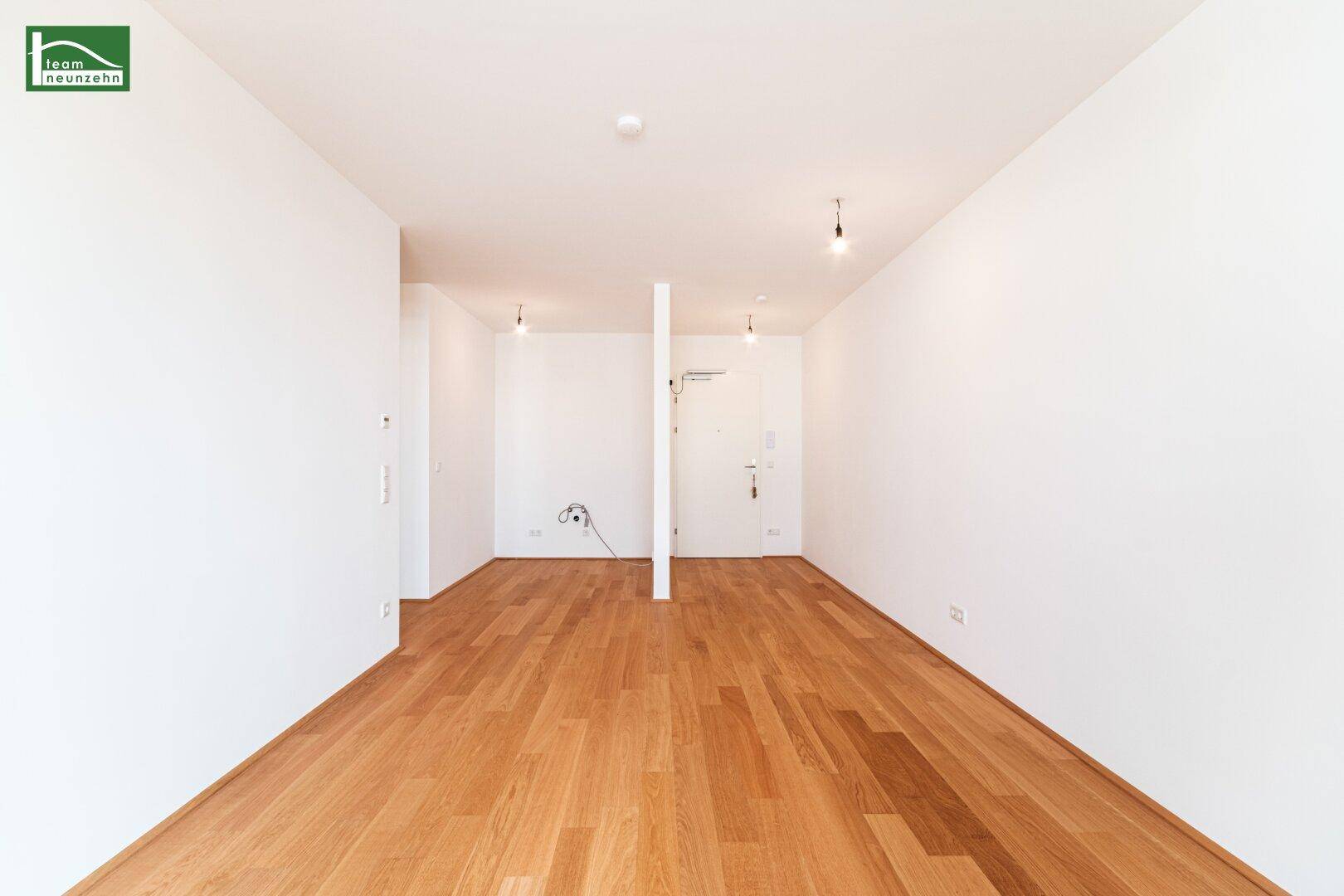 Langer, leerer Flur mit Holzboden und weiß gestrichenen Wänden, führt zur Wohnungstür.