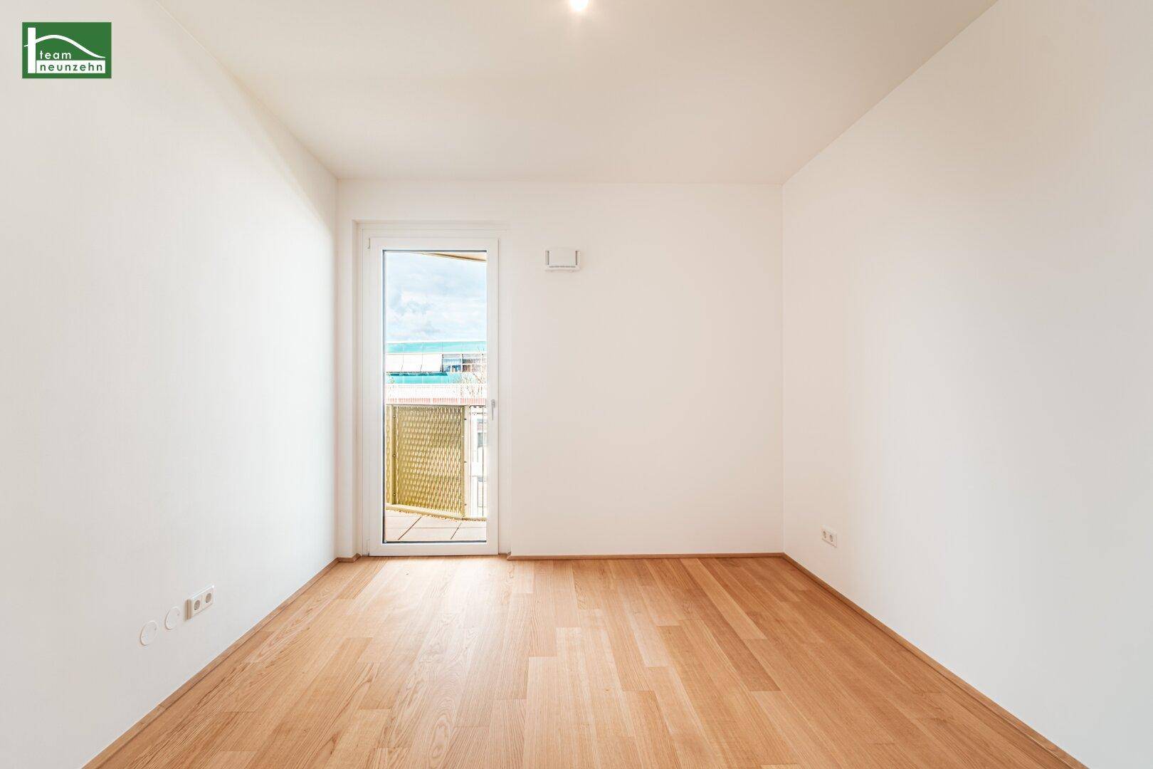 Leeres Schlafzimmer mit Holzboden und Zugang zu einem Balkon, hell und modern.