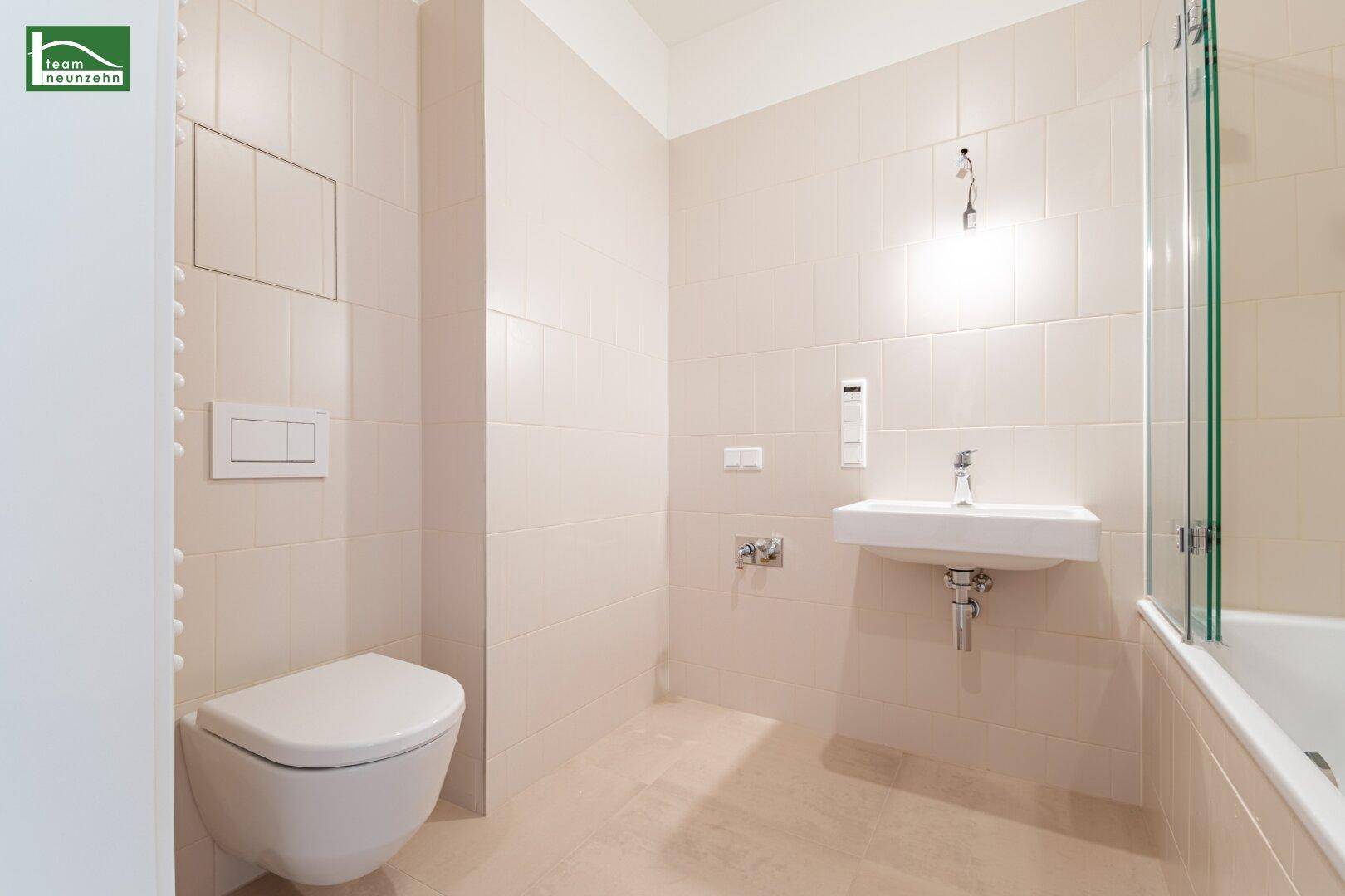 Helles Badezimmer mit wandhängendem WC, Waschbecken und Badewanne, komplett gefliest.
