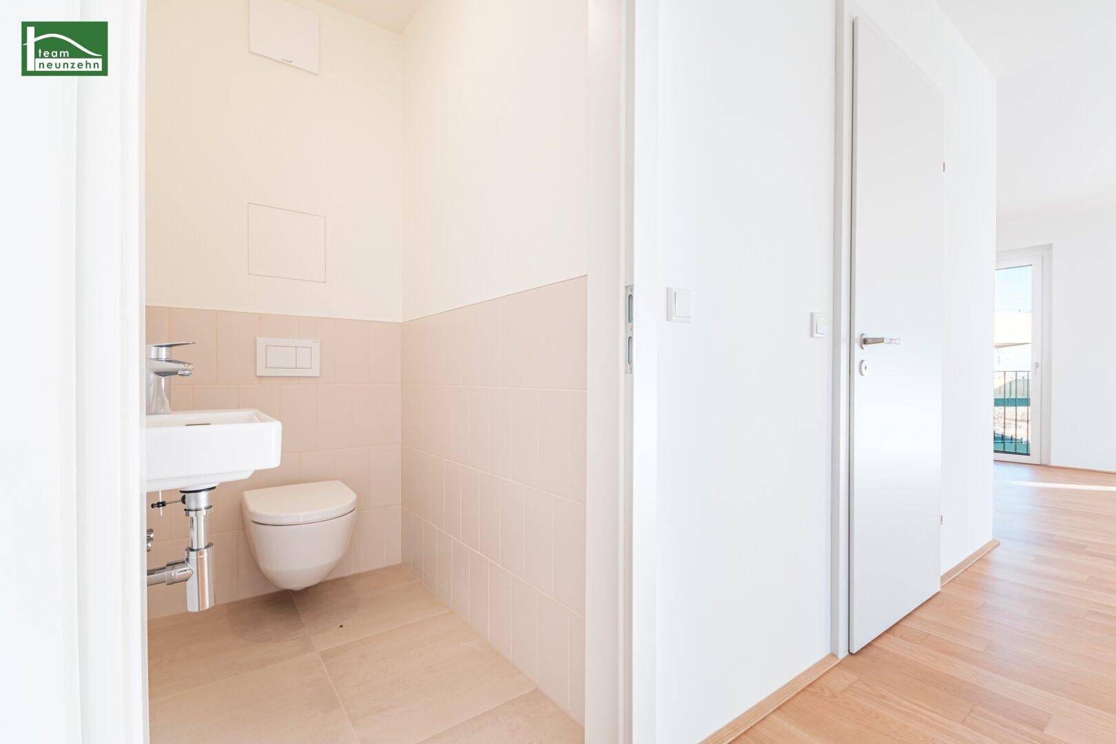 Gäste-WC mit wandhängender Toilette, kleinem Waschbecken und hellen Fliesen.