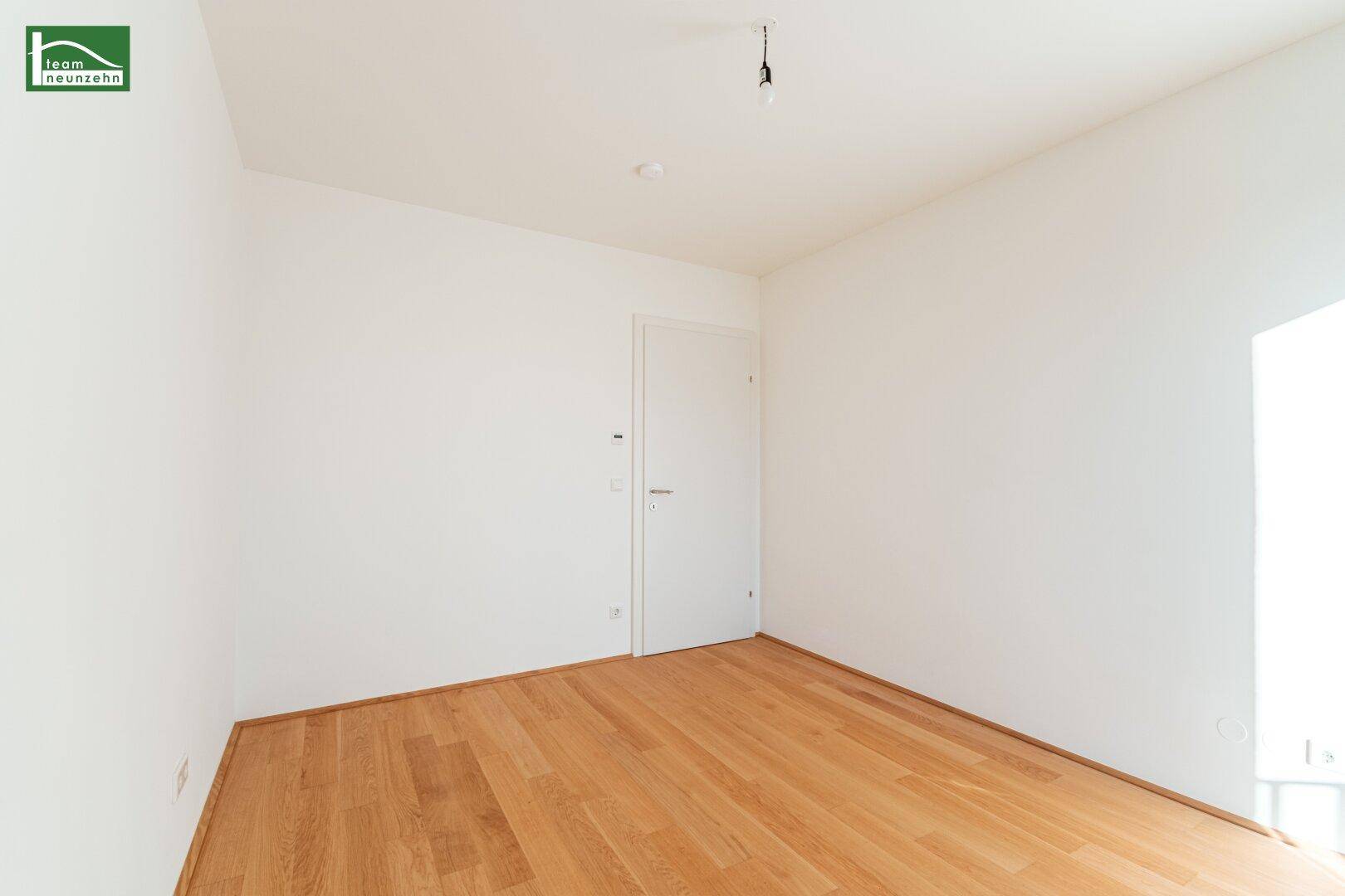 Unmöbliertes Zimmer mit hellem Parkettboden und weißer Tür, bereit zur individuellen Gestaltung.