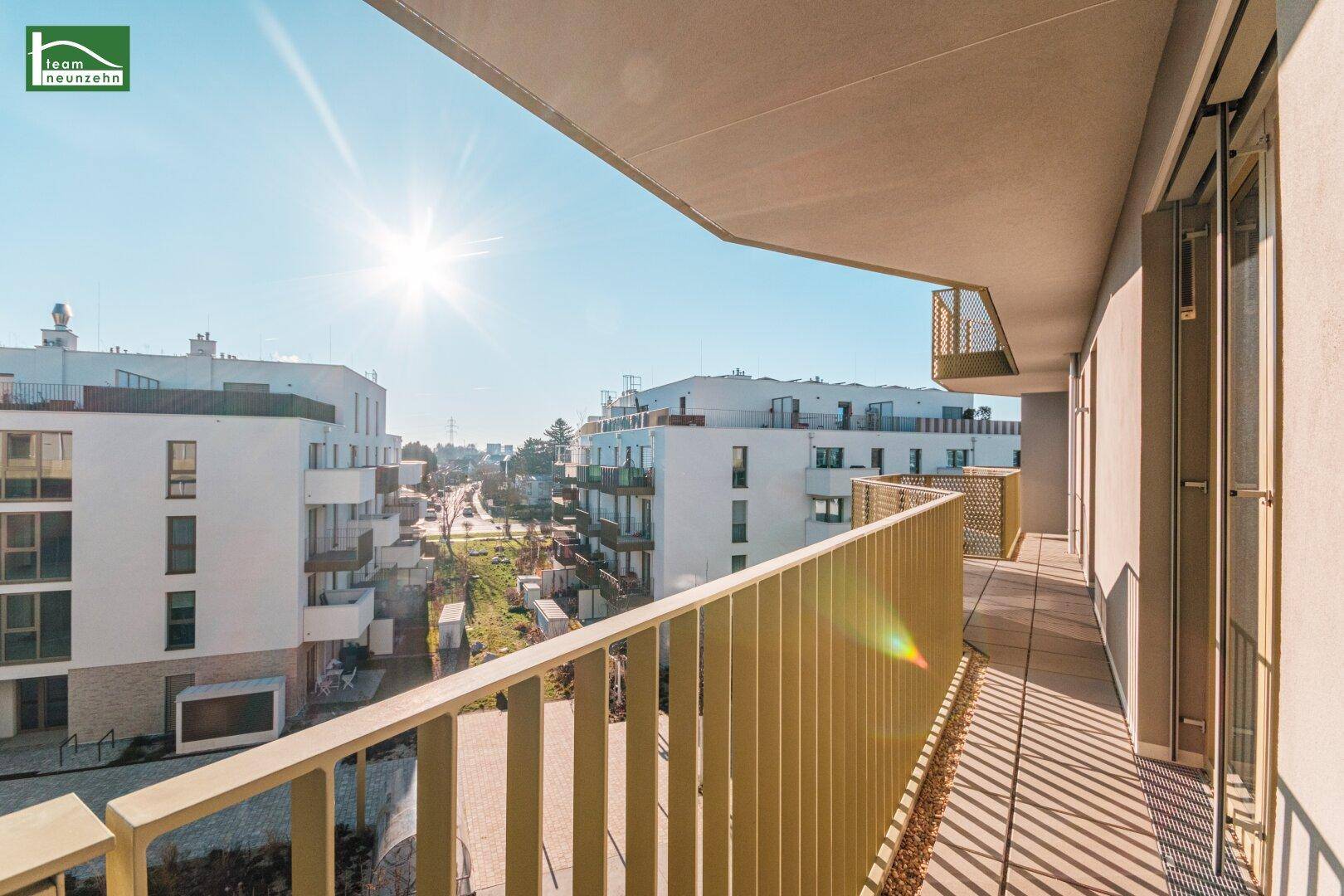 Heller Balkon mit Blick auf die Straße und die umliegenden Neubauten unter strahlendem Himmel.