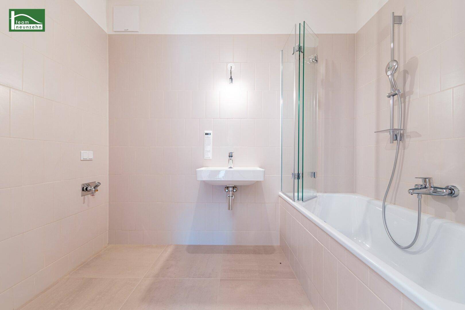 Modernes Badezimmer mit hellbeigen Fliesen, Badewanne mit Duschwand und Einzelwaschbecken.