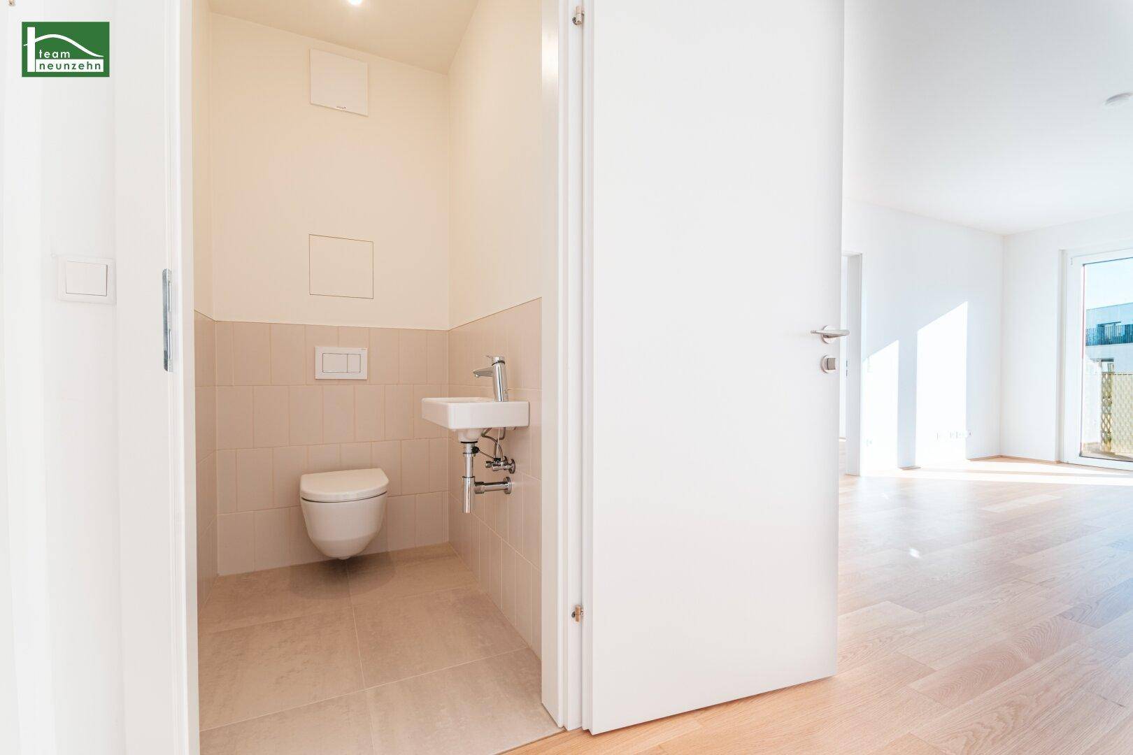 Gäste-WC mit hellbeigen Fliesen, wandhängendem WC und kleinem Handwaschbecken.