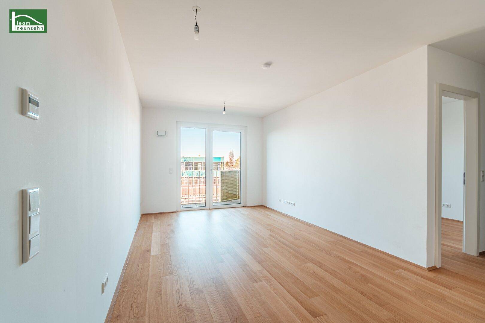 Helles, leeres Wohnzimmer mit Holzboden und Zugang zu einem französischen Balkon.