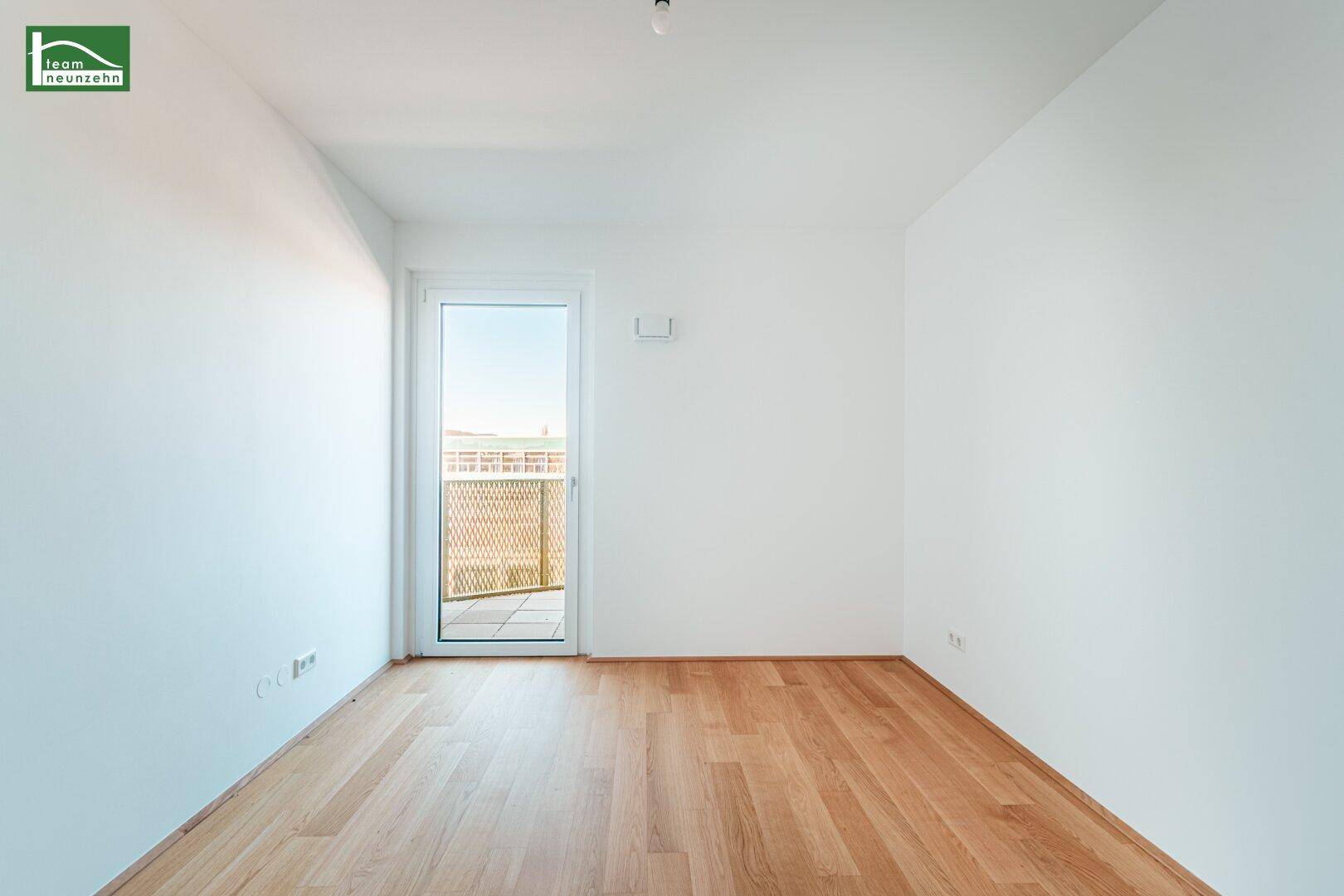 Leeres Schlafzimmer mit Holzboden und Zugang zu einem Balkon, bietet viel Tageslicht.