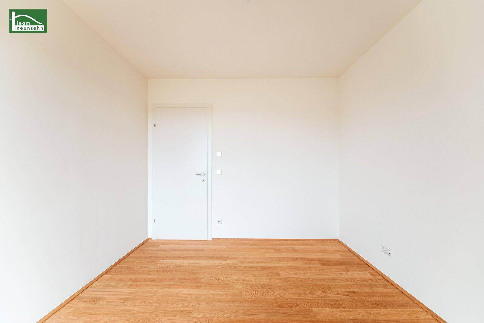 Unmöblierter Raum mit Holzboden und einer schlichten weißen Tür, vielseitig nutzbar.