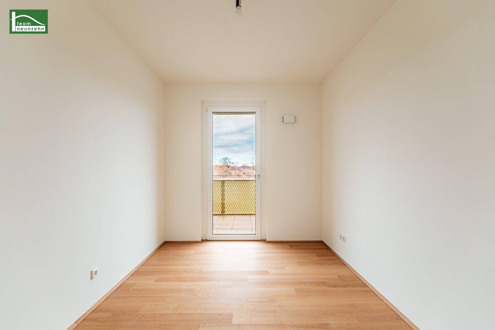 Kleineres Zimmer mit Holzboden und einer Tür, die zu einem Außenbereich führt, ideal als Schlafzimmer.