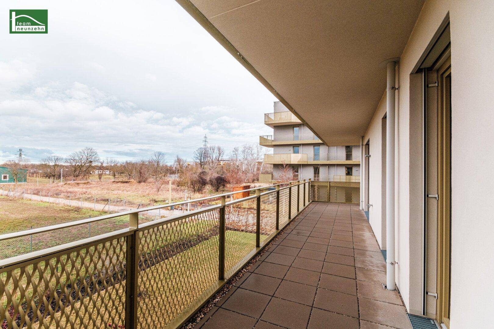 Großer Balkon mit Metallgeländer und weitem Blick auf die umliegende Natur und Wohnbebauung.