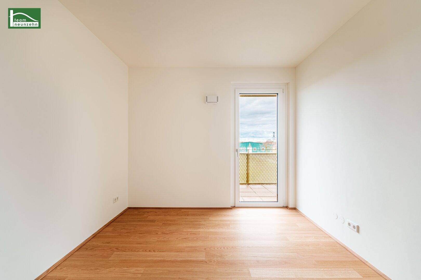 Unmöbliertes Zimmer mit Holzboden und Zugang zu einem Balkon, bietet viel natürliches Licht.