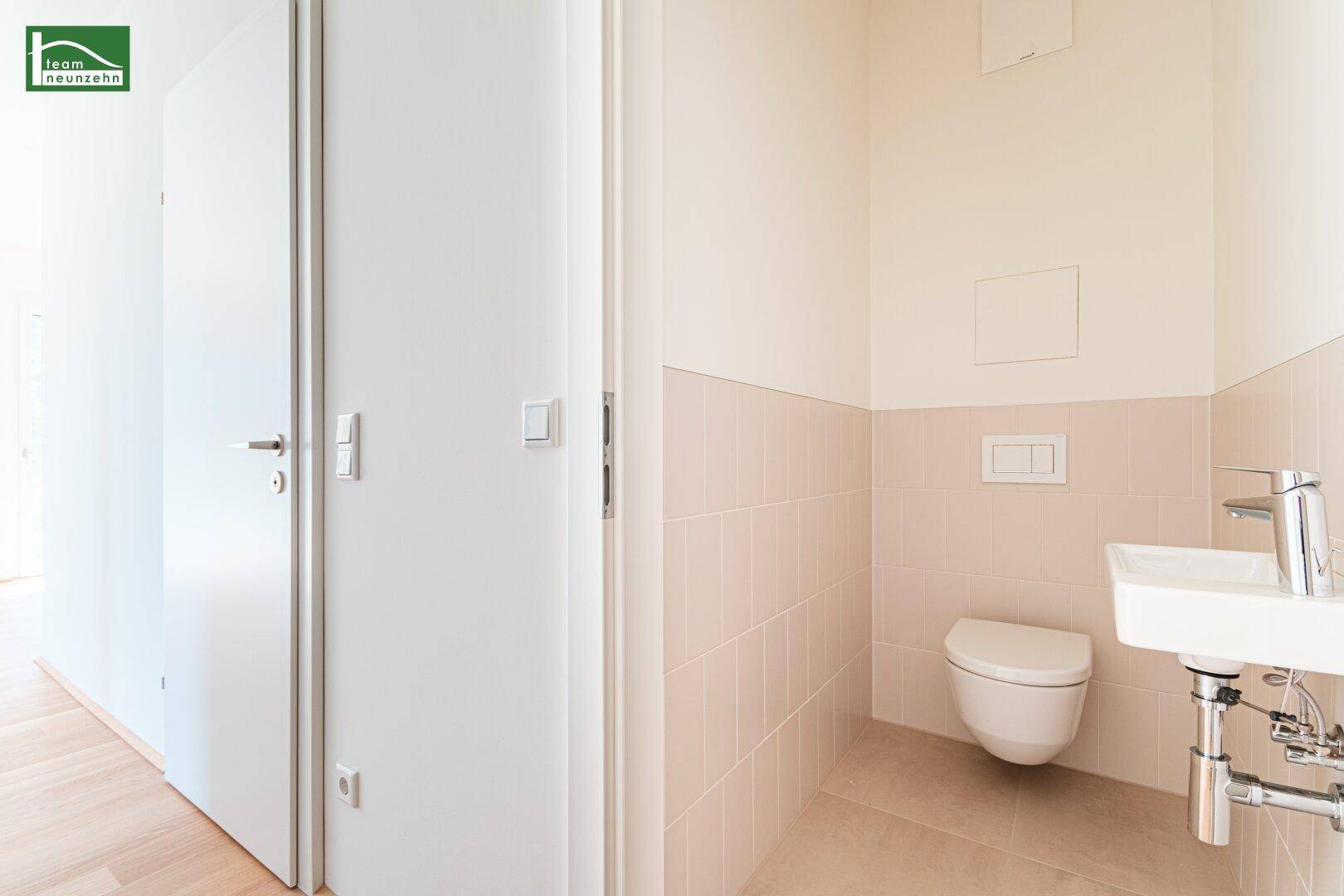 Separates Gäste-WC mit wandhängender Toilette und kleinem Waschbecken, modern gefliest.