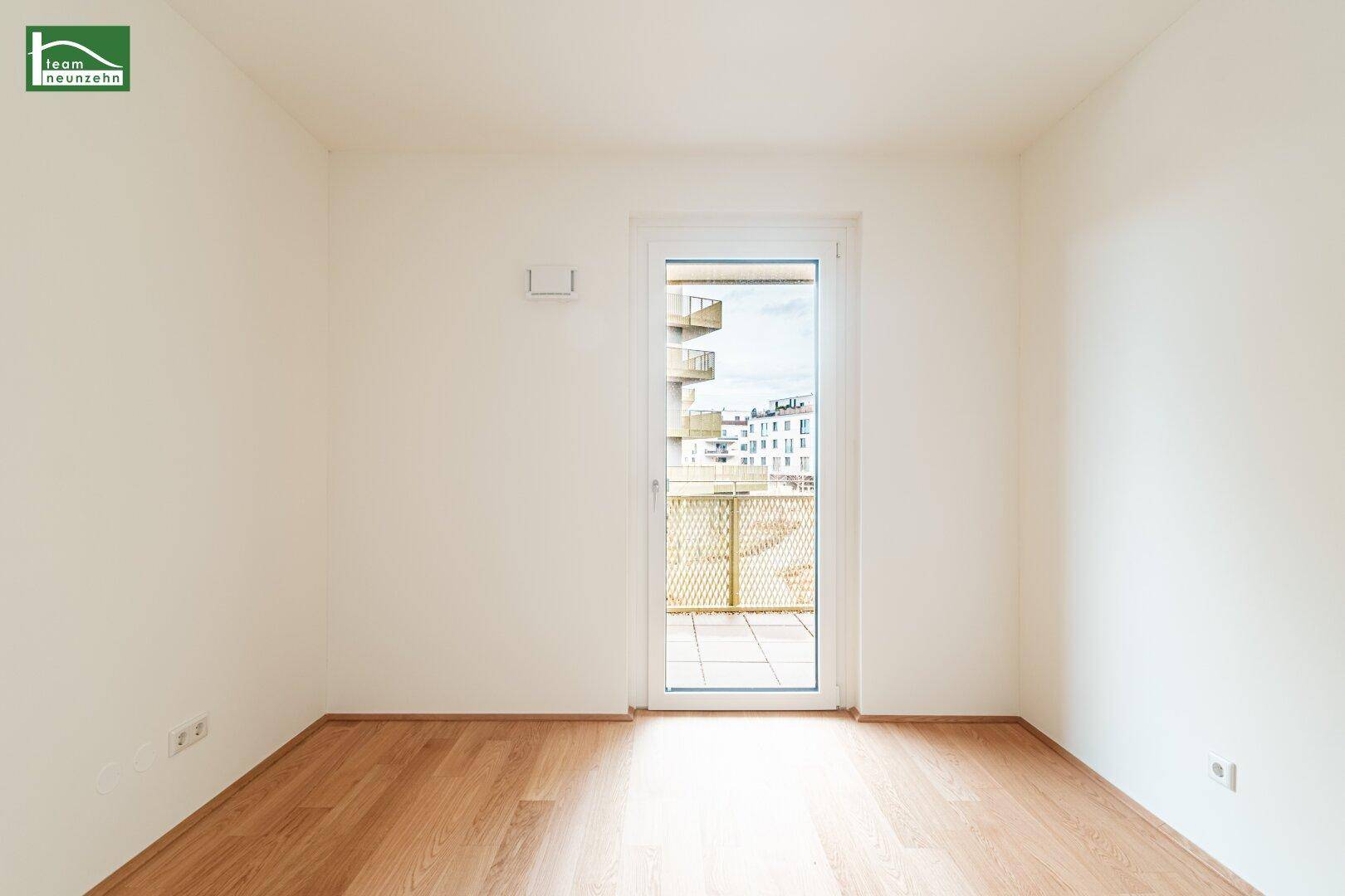 Leeres Zimmer mit Holzboden und einer Tür, die auf den Balkon führt.