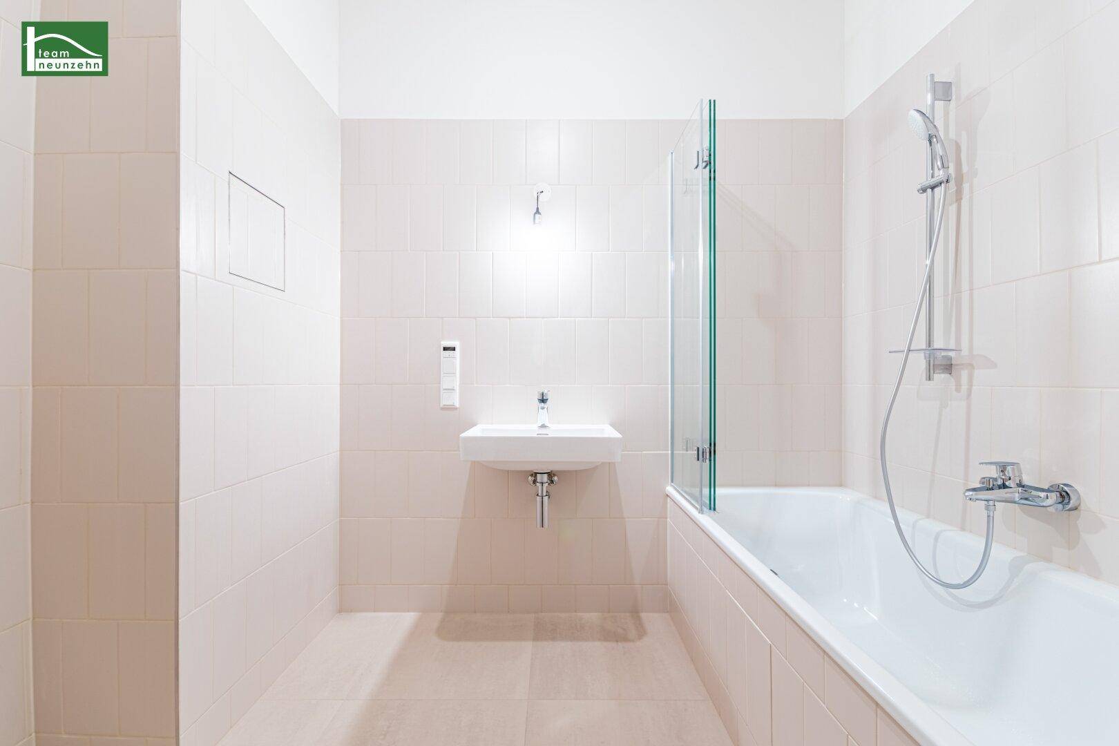Modernes Badezimmer mit hellen Fliesen, Badewanne mit Duschwand und Einzelwaschbecken.